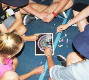 A picture of students creating a symbol of compassion together on a mini blackboard which is an example of an engaging activity from one of Donna Power's school retreat programs which you can enquire about on this page from her Experience Wellbeing website